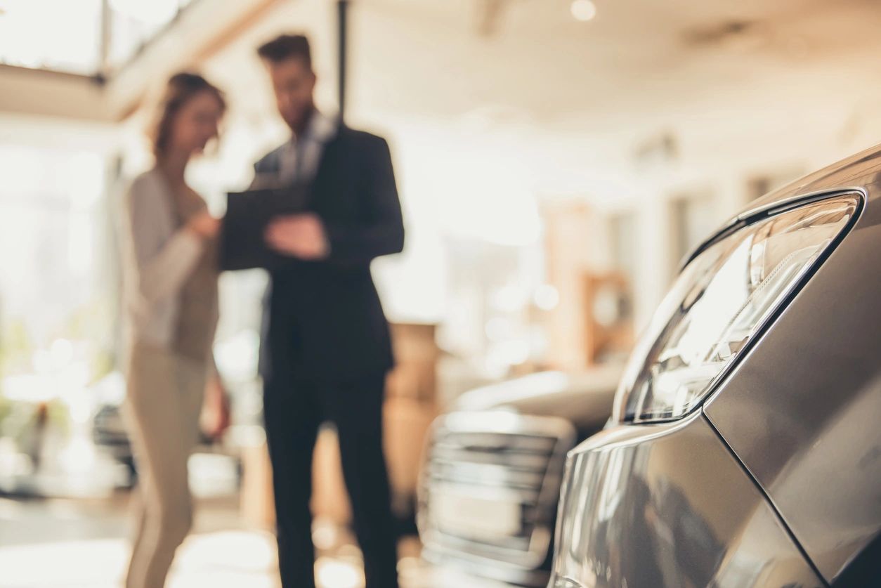 fm=f_5ZzWgB0 A man and woman in suits standing next to a car.